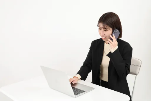 電話で相談しながらノートパソコンを操作する女性