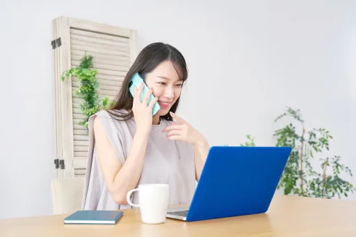 自宅で電話をしながらノートパソコンを見る女性